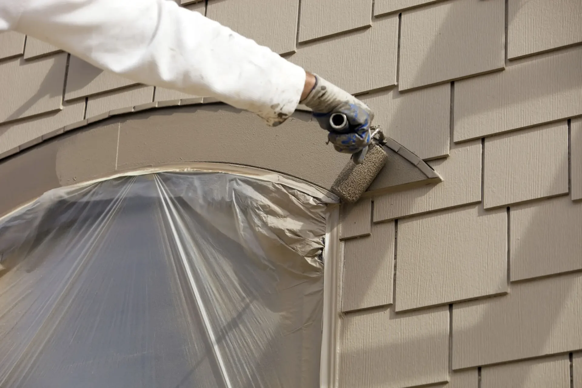 Painting exterior shingles with a roller brush.