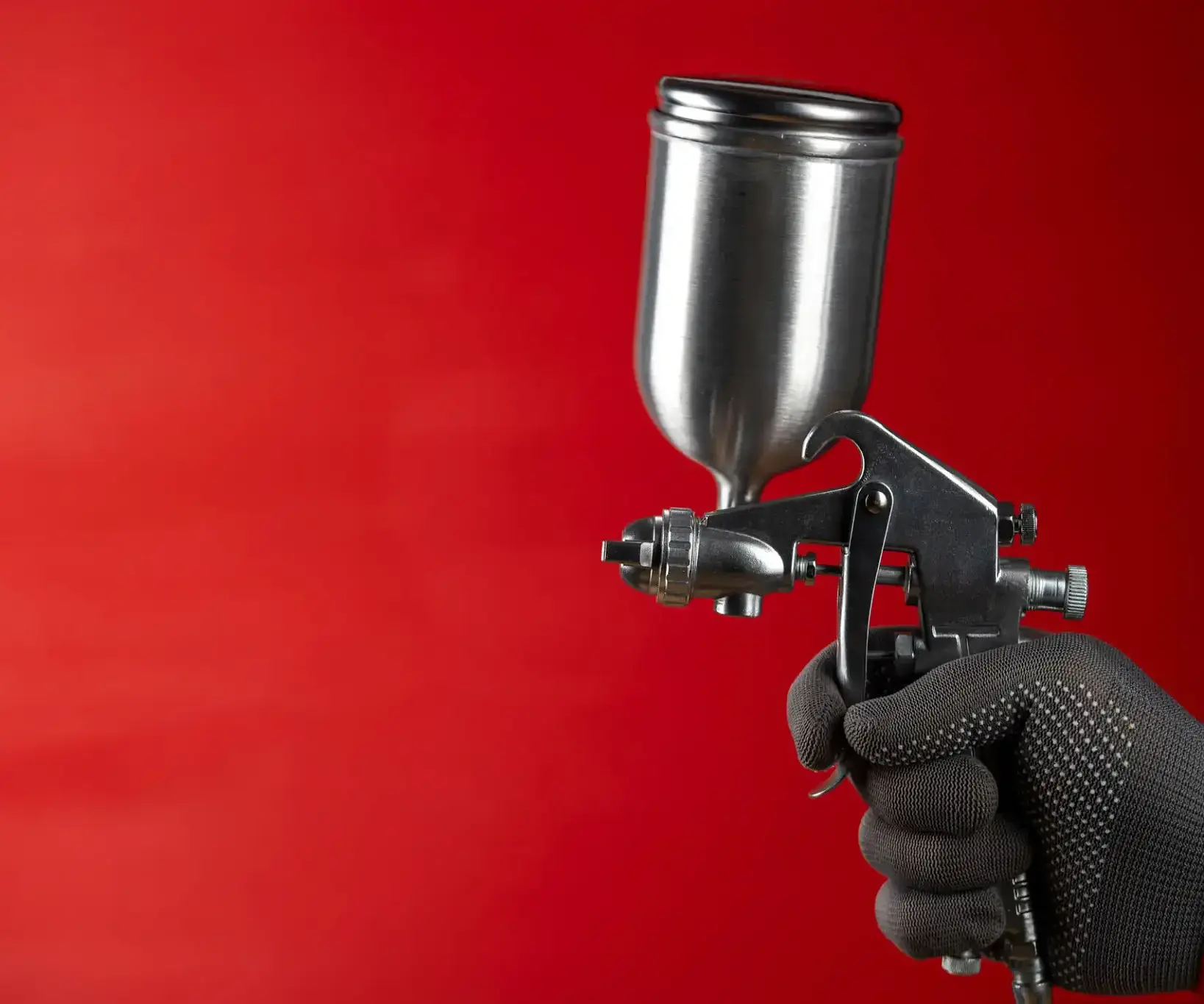Hand holding spray gun on red background.