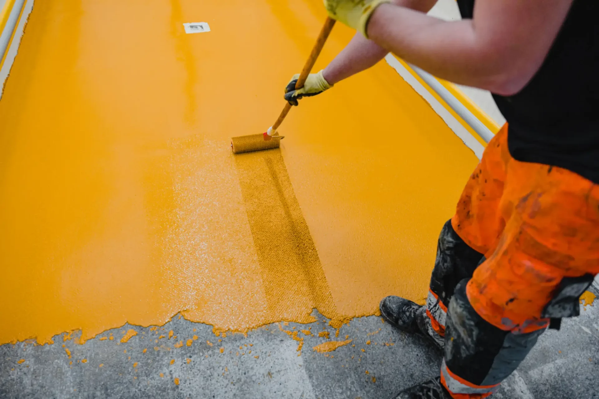 Worker painting floor with orange epoxy resin.