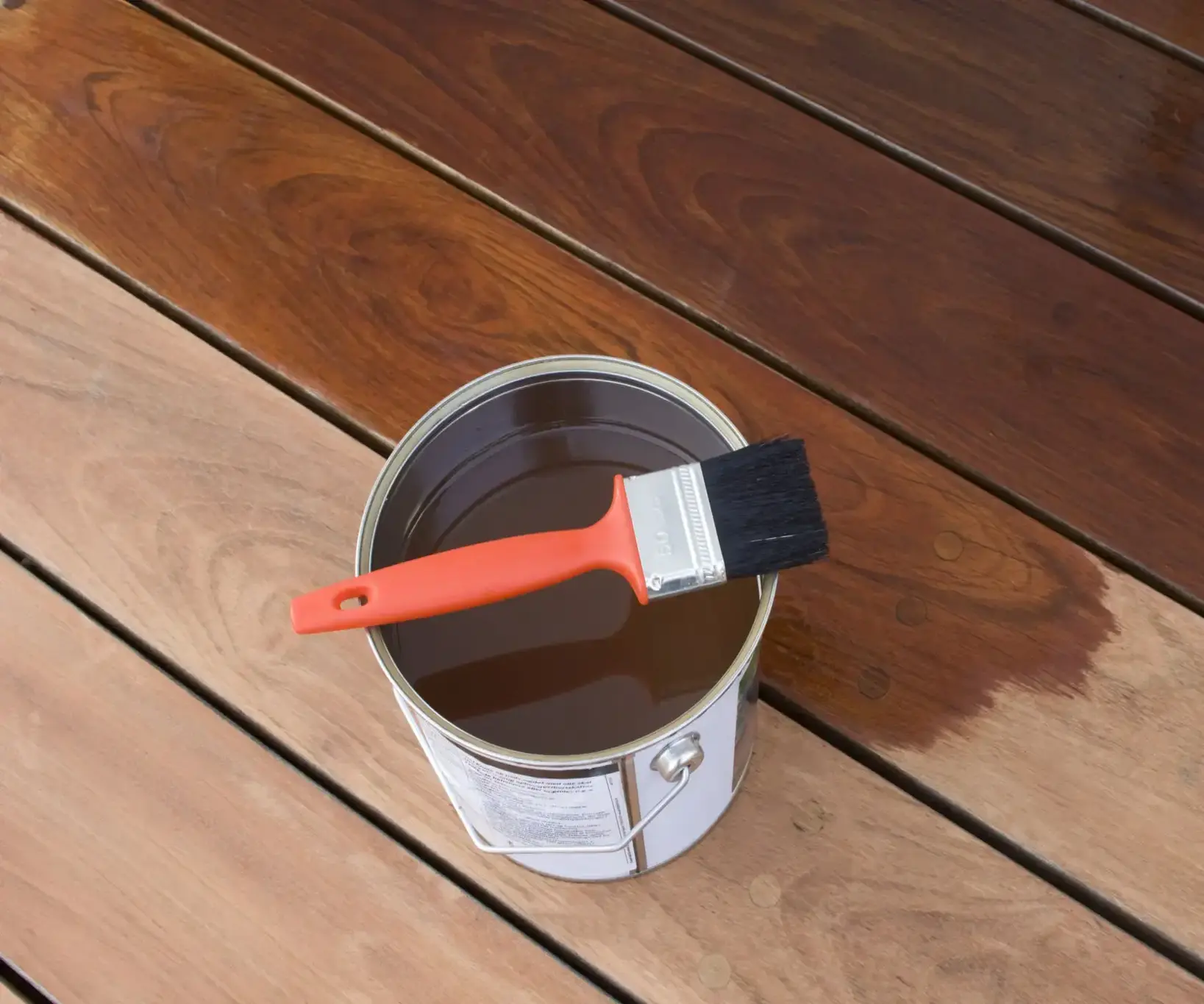 Paint can and brush on wooden deck.