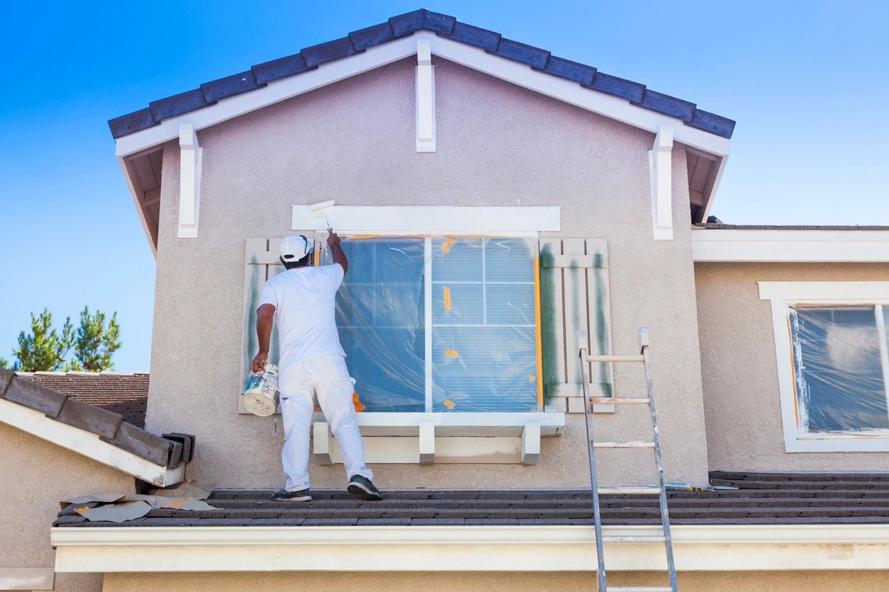 Worker painting the exterior wall of a house on a ladder.